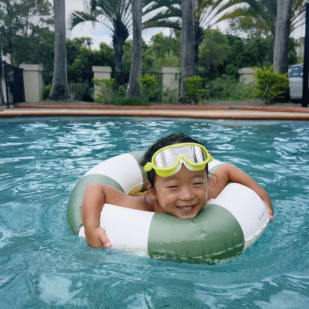 Child in a pool with a green and white inflatable ring and goggles