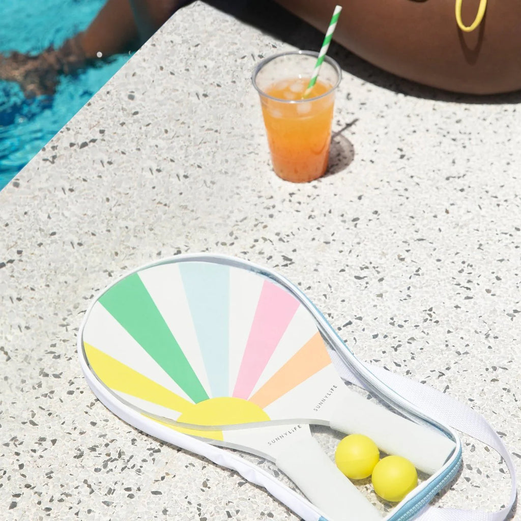 Colorful paddle with two balls on a concrete surface next to a pool.