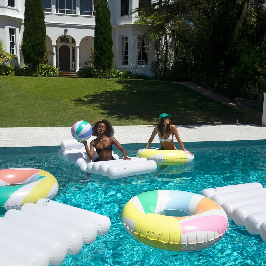 Two women on inflatable pool toys in a pool with a house in the background