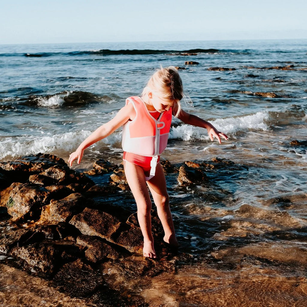 Child playing on rocks by the ocean with a life jacket on