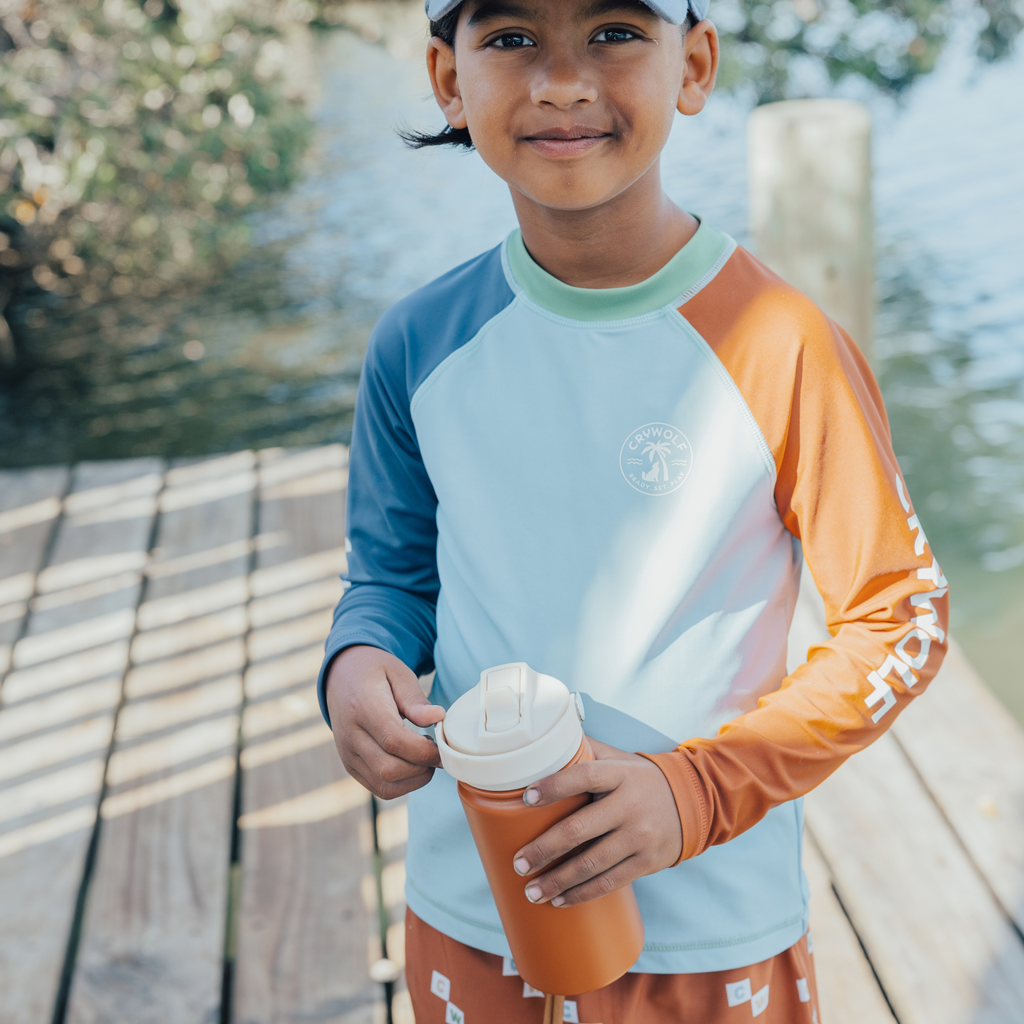 Boy on a jetty holding a brown colour sippy water-bottle with the text "crywolf" in white text with a wolf outline and a white coloured lid