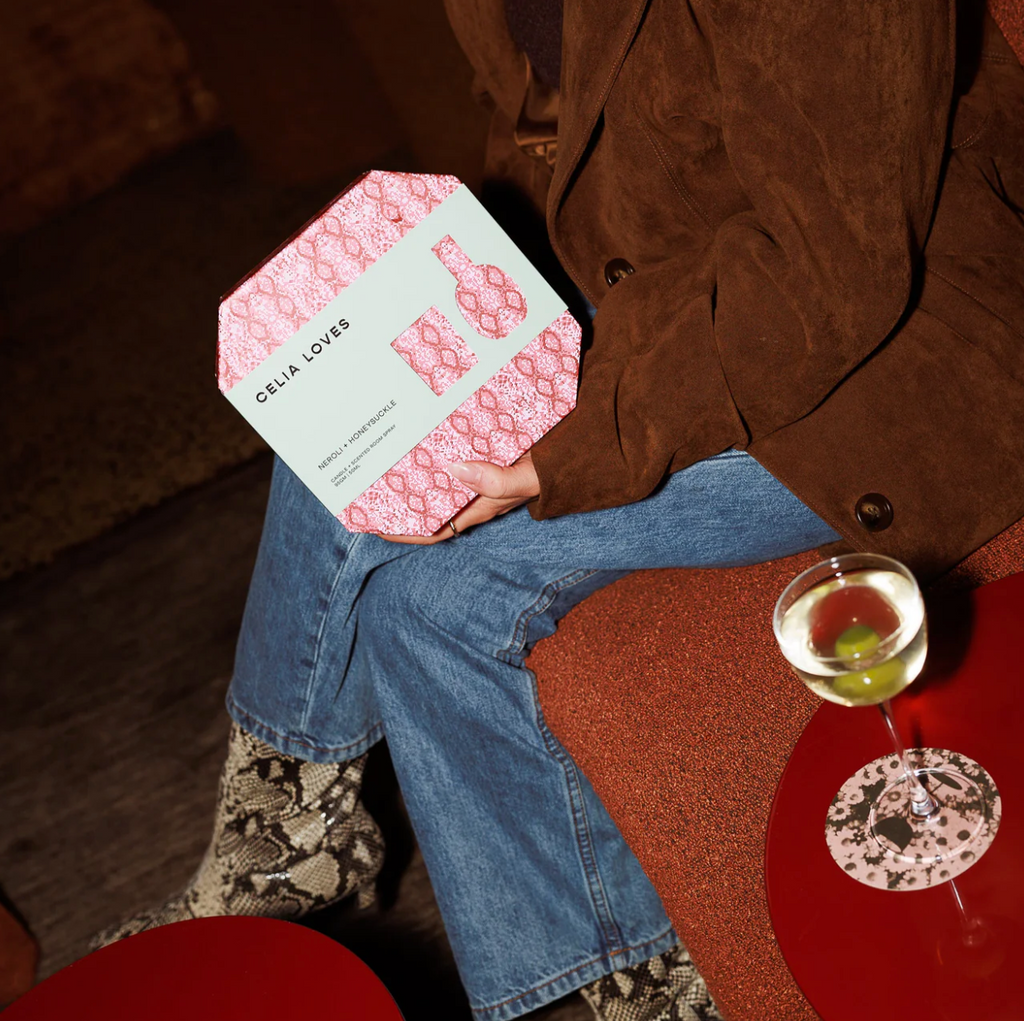 Person sitting on a couch holding a box with a drink on a table next to them.