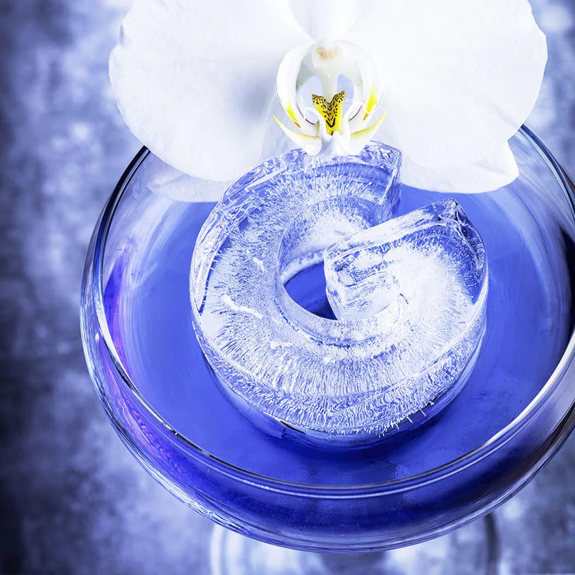 Clear ice cube with a unique design in a glass of blue liquid, garnished with white flowers.