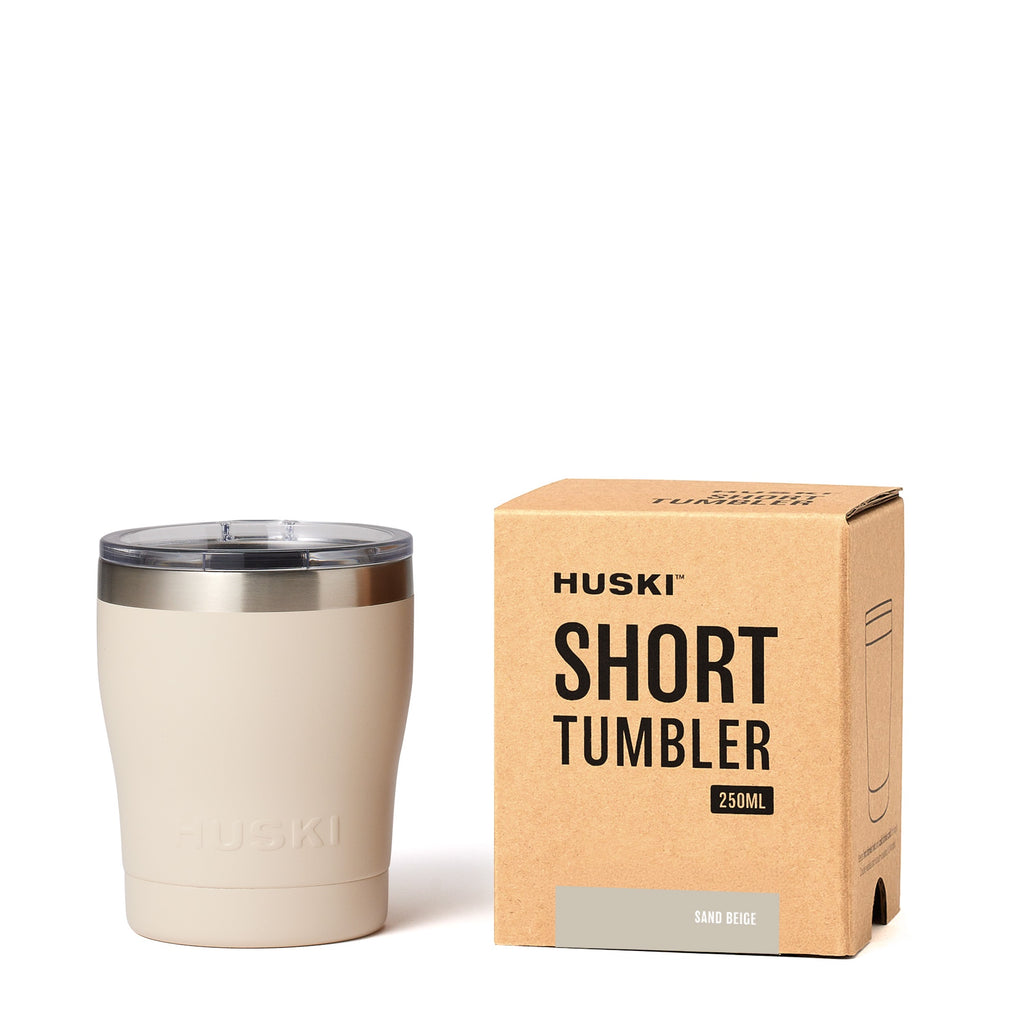 Beige tumbler with silver rim next to its packaging box on a white background