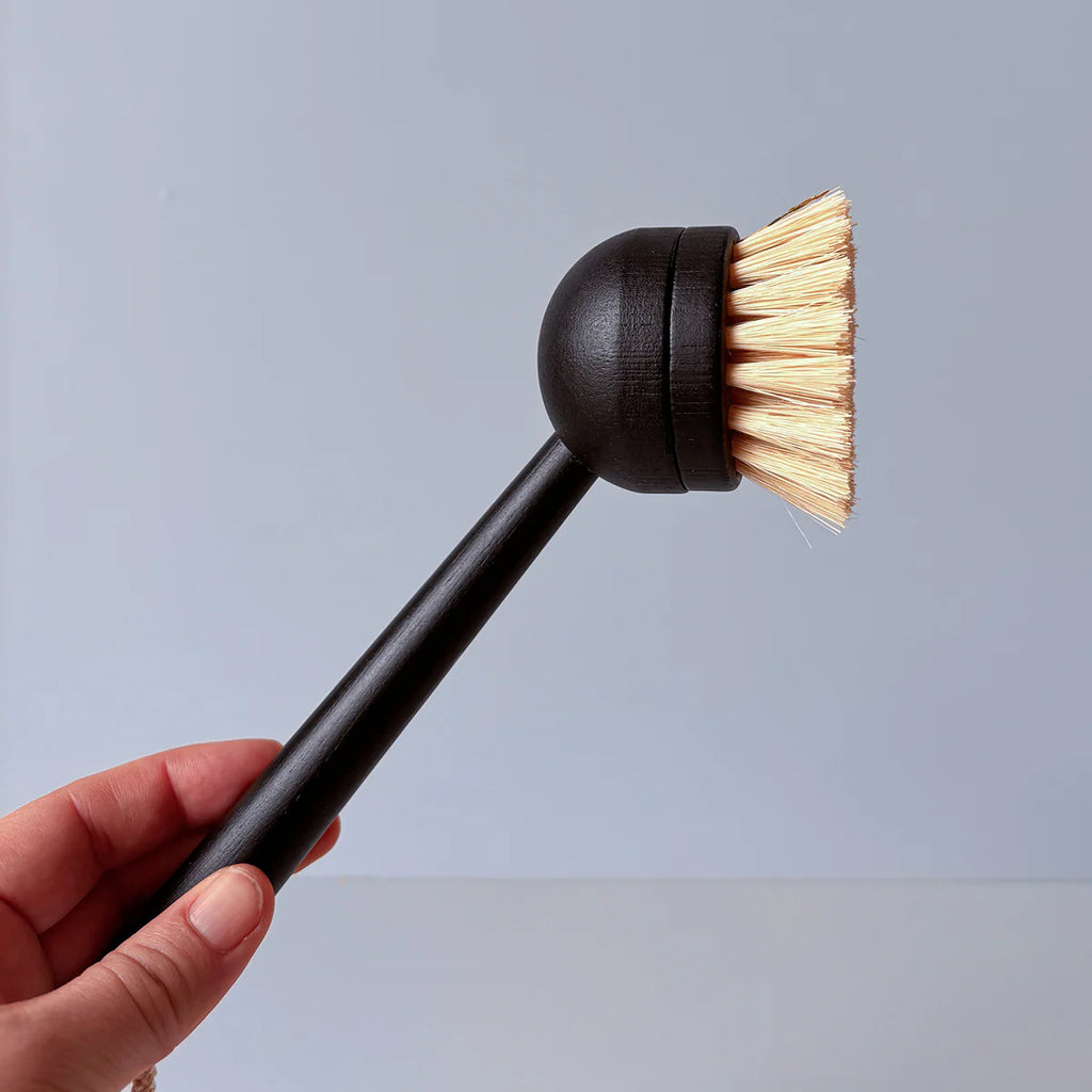 Hand holding a black scrubbing brush with bristle head against a light gray background