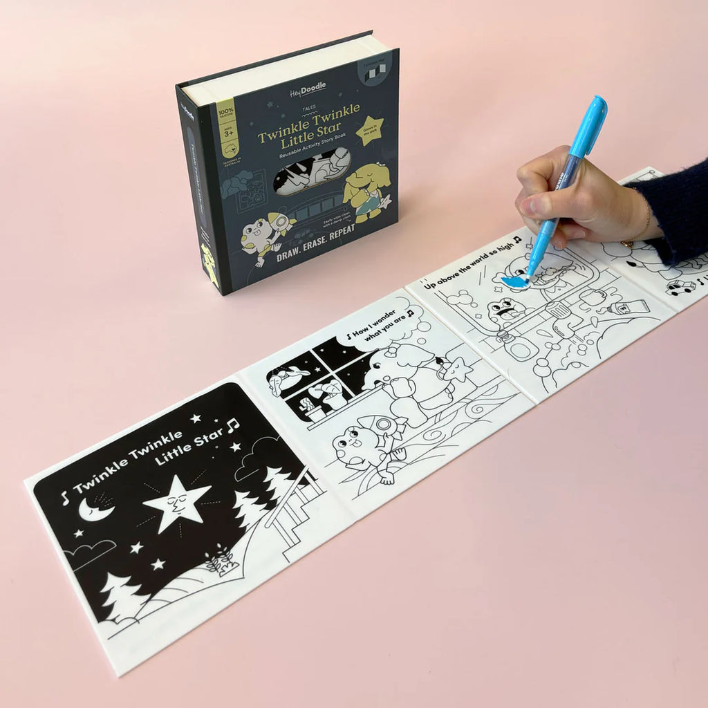 Coloring book with black and white illustrations and a hand holding a blue pen on a pink background