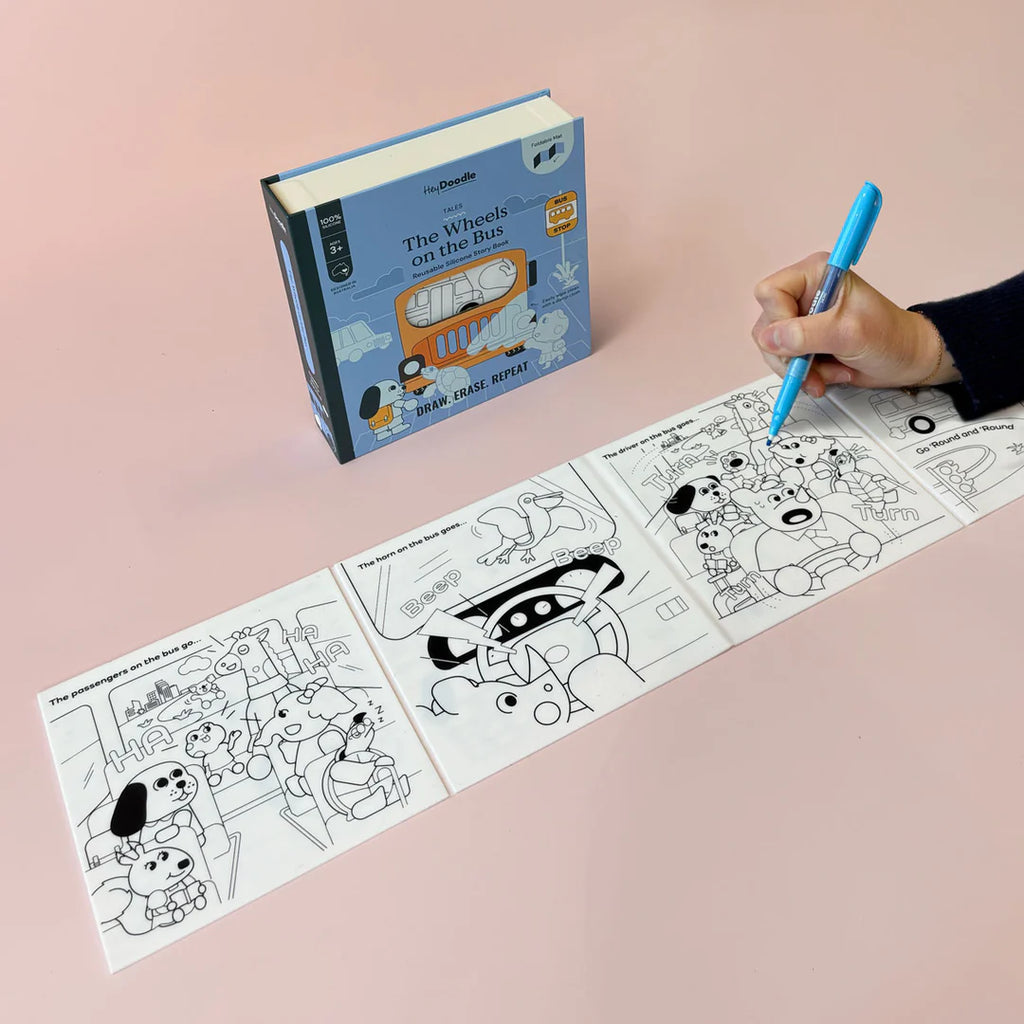 Coloring book with 'The Wheels on the Bus' and a hand holding a pen on a pink background