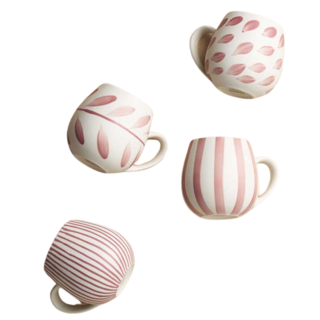 A set of four rounded shape mugs with various painted patterns in pink paint with a handle on a white background