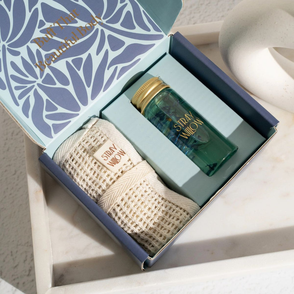 Gift box with a large weave fabric cloth and glass bottle with body oil. Box is open on a tray