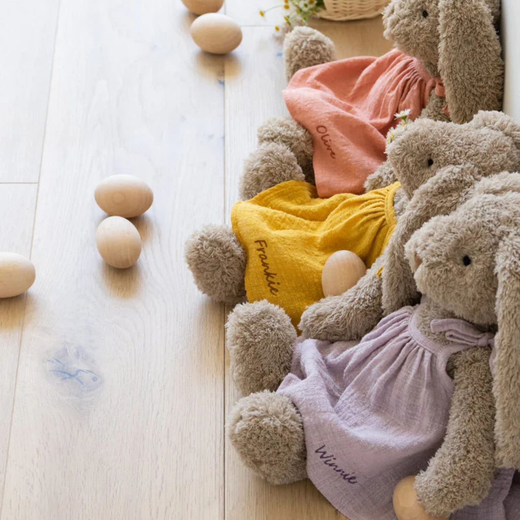 three soft toy bunnies sitting against a wall wearing different coloured dresses