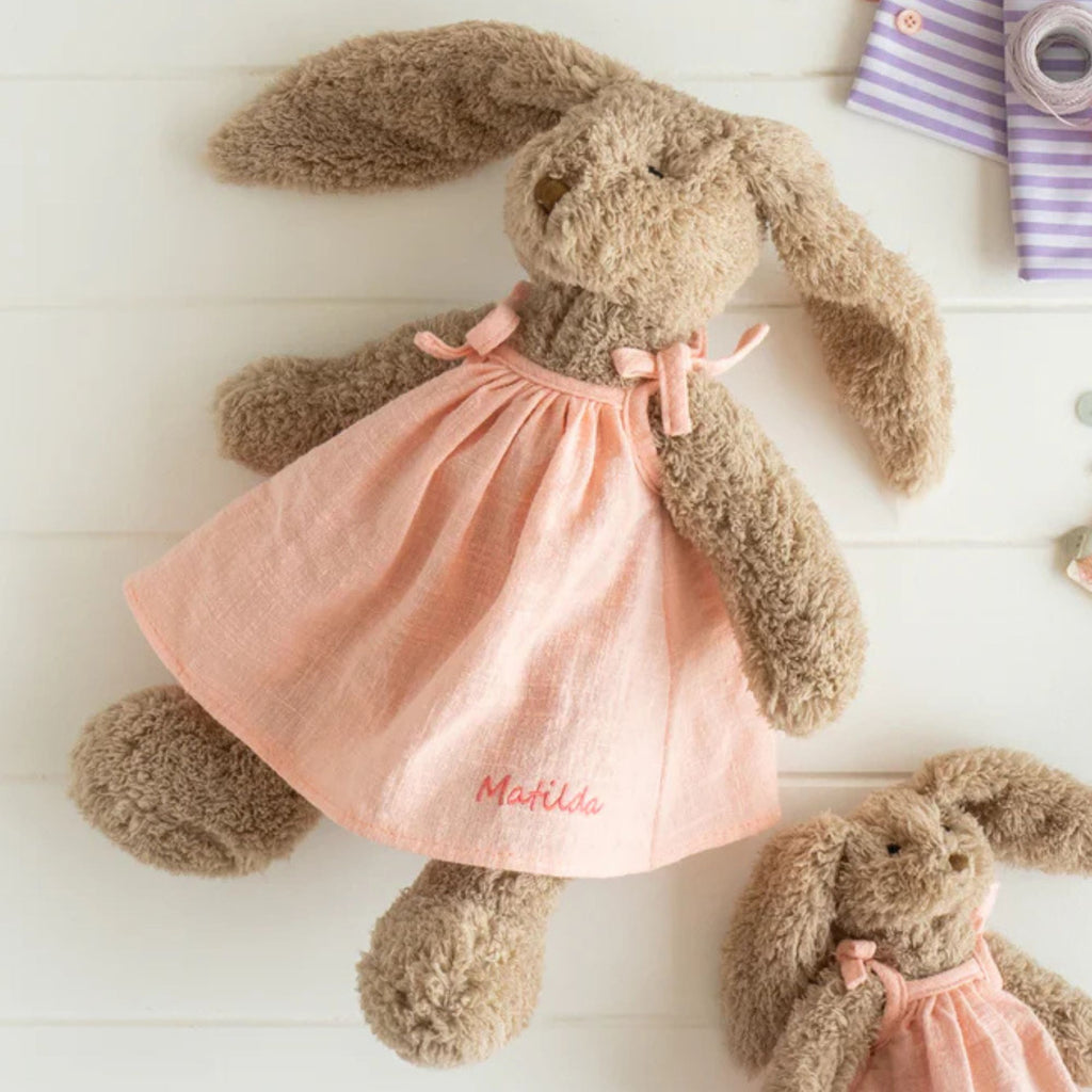 A plush toy rabbit wearing a baby pink dress with the name 'Matilda' embroidered on it,