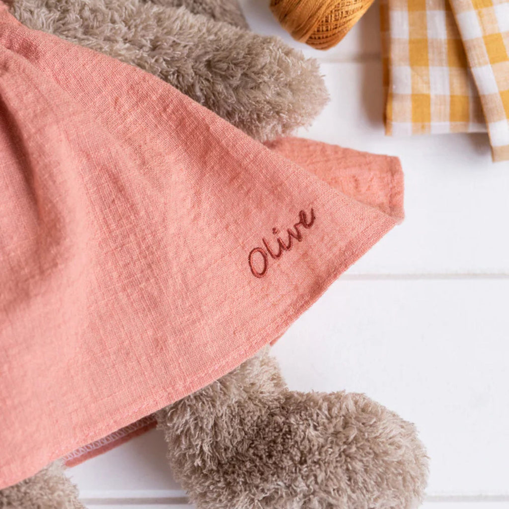 close up detail of a soft toy bunnies clothing with the name olive on it