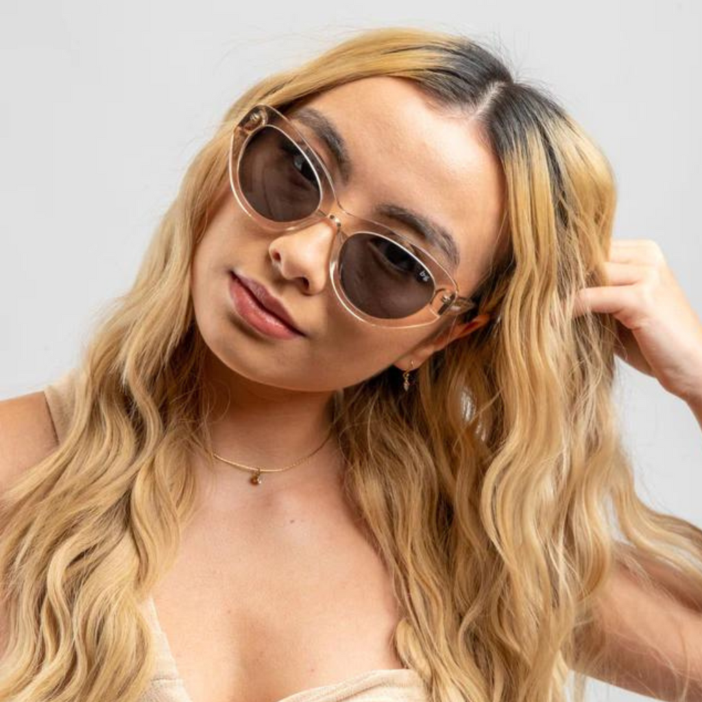 A woma weating Bored George Demi pink sunglasses with a clear pink frame and dark lens with her head tilted 