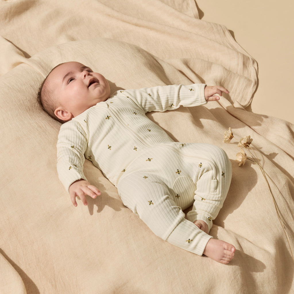 Baby lying on a beige blanket wearing a white onesie with small patterns.