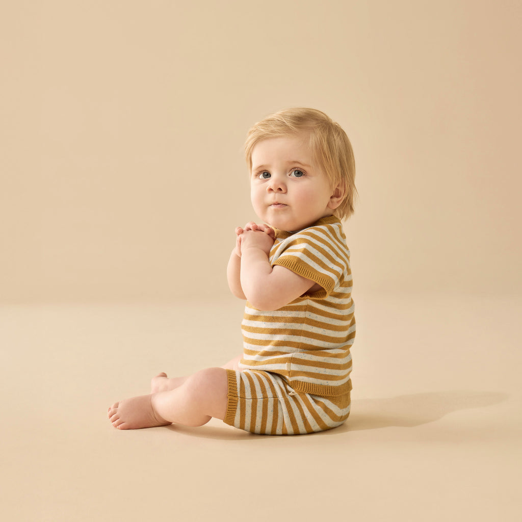 Baby wearing a yellow and brown striped outfit sitting on a beige background