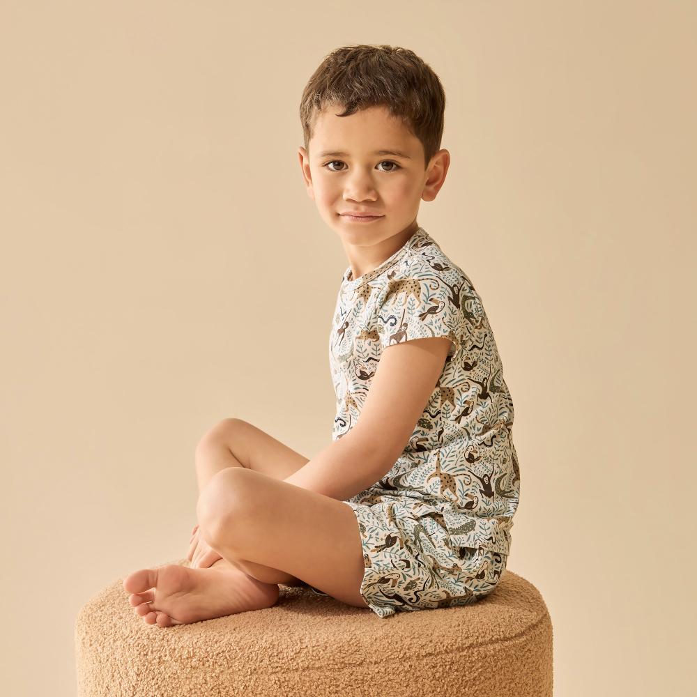 Child wearing a patterned outfit sitting on a beige stool against a beige background