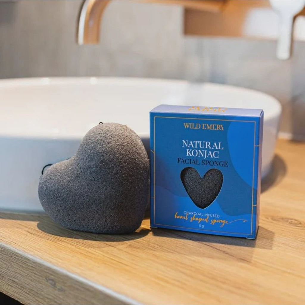 Natural Konjac Sponge - Charcoal Infused. Blue box next to charcoal heart shaped sponge. in front of a bathroom sink