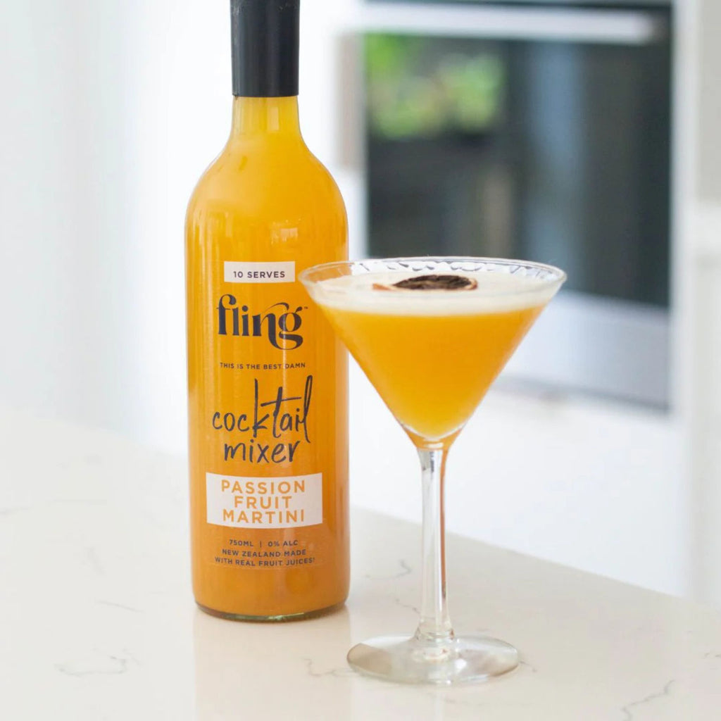 Bottle of Fling cocktail mixer next to a cocktail glass filled with a yellow-orange drink.