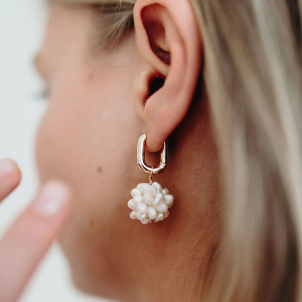 Close-up of a gold hoop earring with a pearl drop worn by a person.