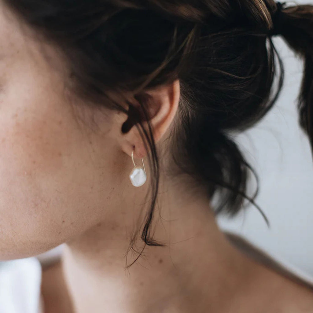 Close-up of a person wearing pearl earrings with a blurred background
