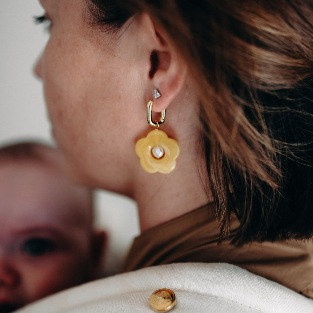 Close-up of a woman wearing a yellow flower-shaped earring with a blurred background