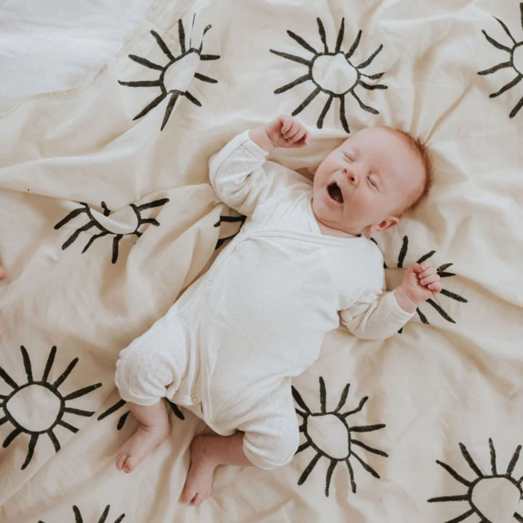 Baby lying on a white blanket with black sun patterns