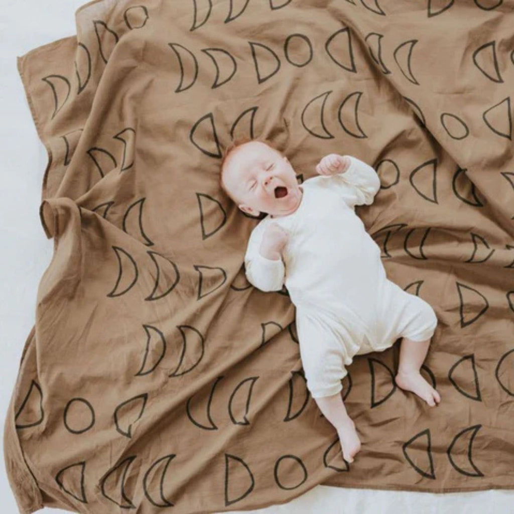 Newborn baby lying on a brown blanket with black patterns