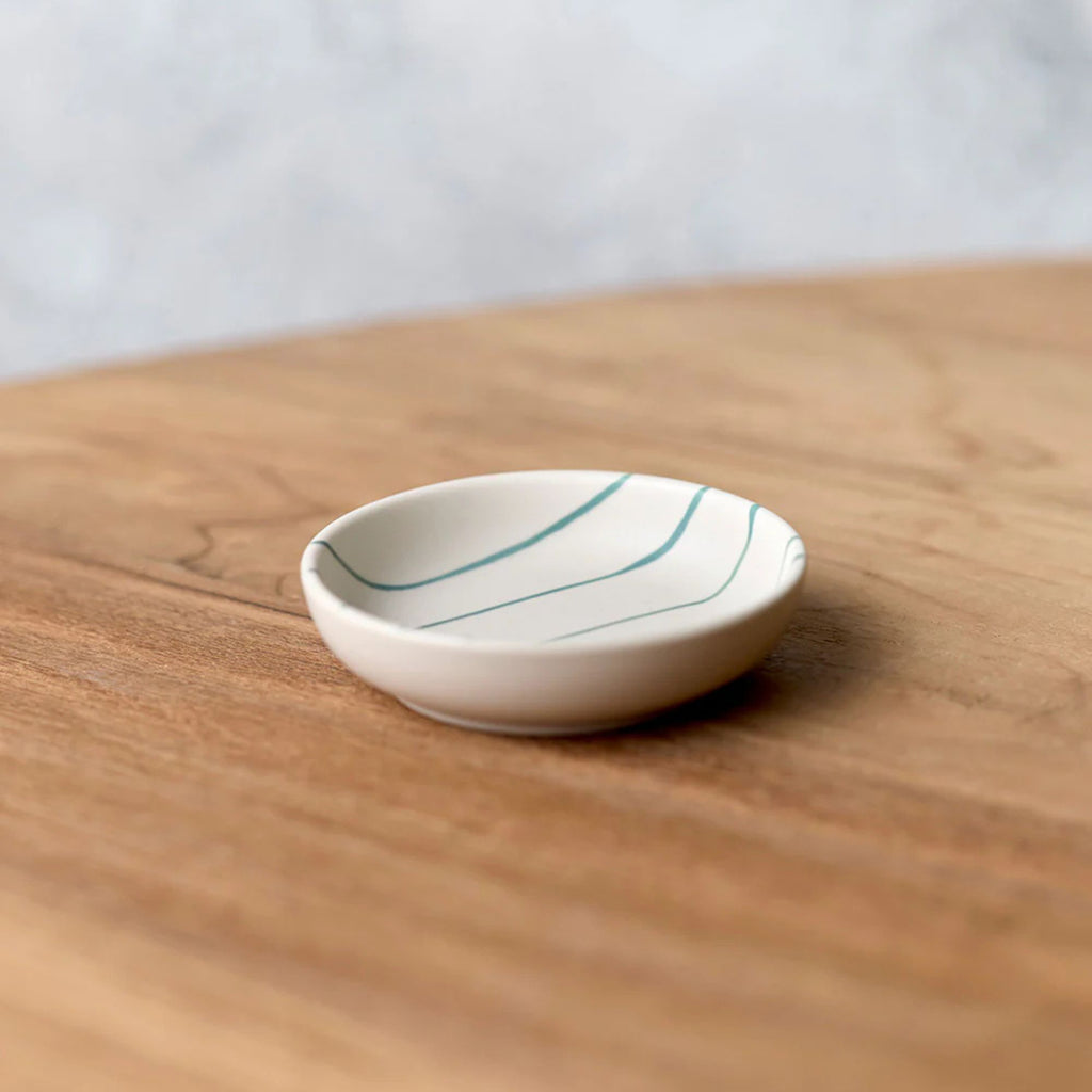 Small white ceramic dish with blue lines on a wooden surface