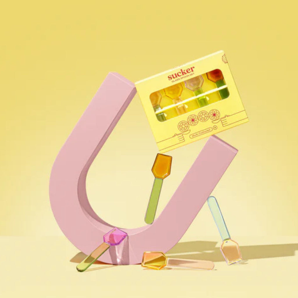 Pink U-shaped holder with colorful glass spoons on a yellow background