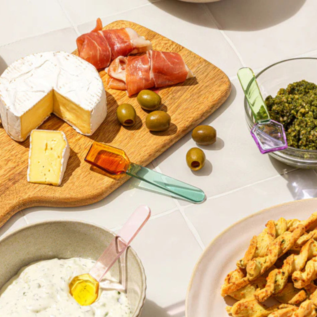 Assorted cheese, olives, and cured meats on a wooden board with a side of bread and dip.