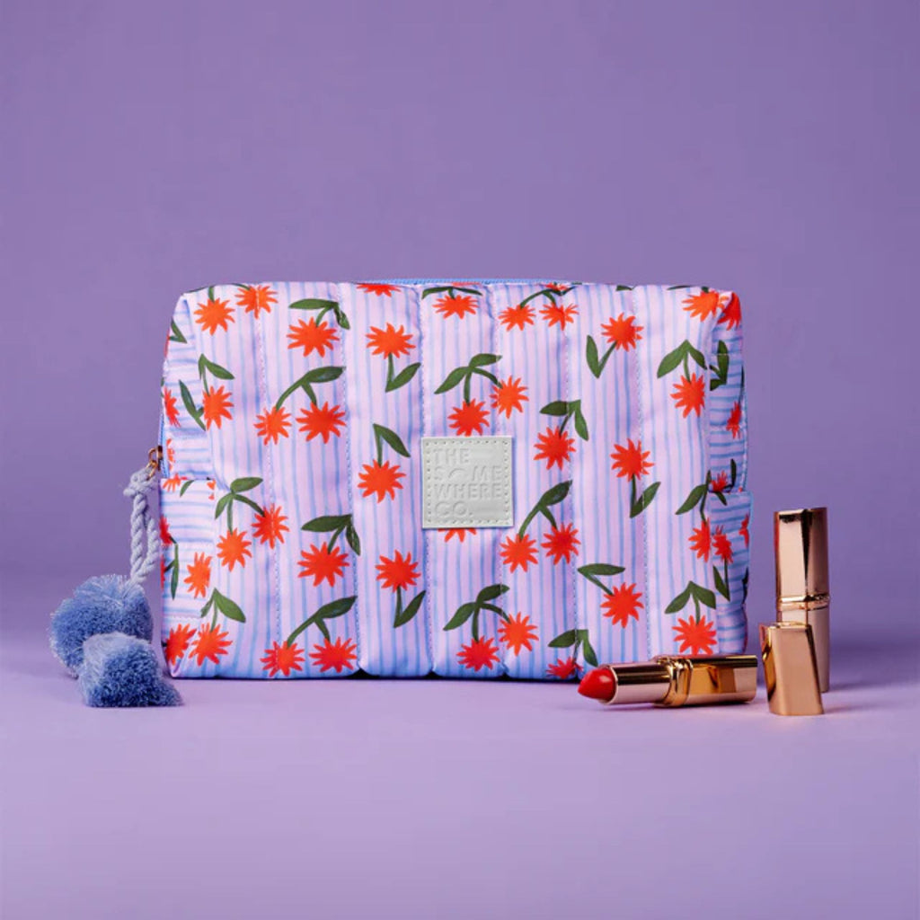 Floral-patterned pouch with a pom-pom and lip balm on a purple background