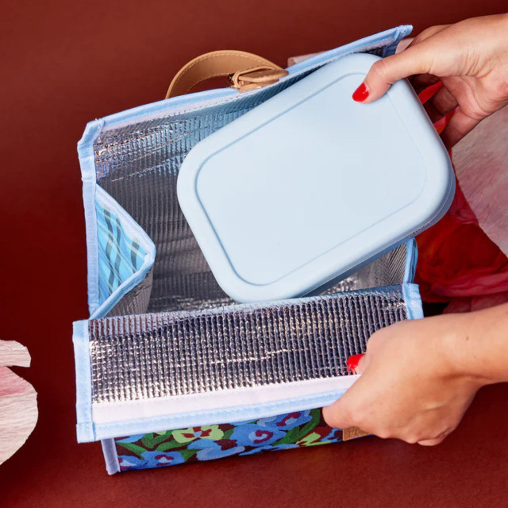 Person holding a colorful lunch bag with a blue lunchbox on a red background