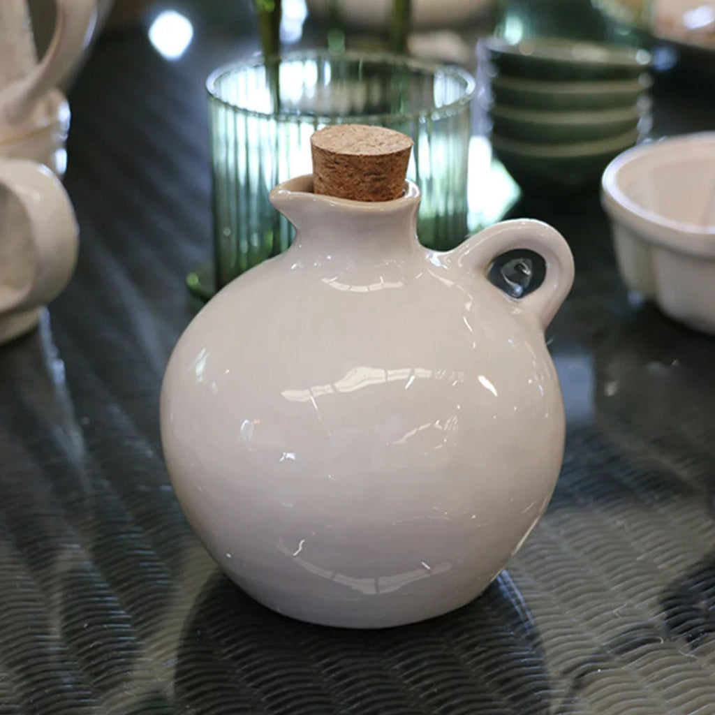 white ceramic oil jar with cork lid on a reflective surface