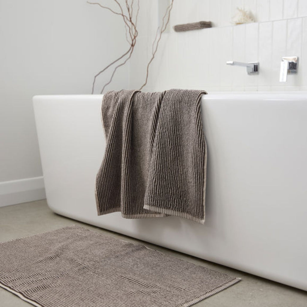 Brown textured towel draped over a white bathtub in a bathroom setting.