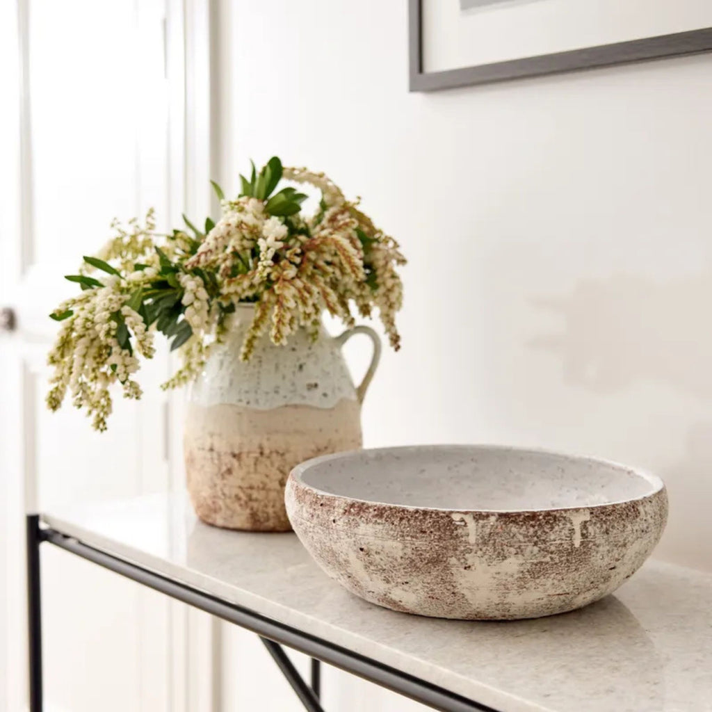 Decorative bowl and vase with flowers on a table against a white wall.