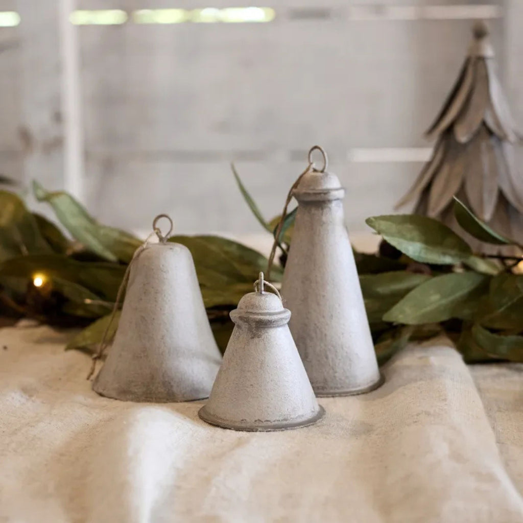 Three rustic metal bells on a textured surface with greenery in the background