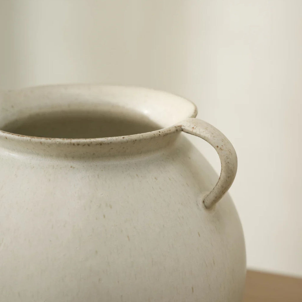Close-up of a ceramic jar with a handle on a neutral background
