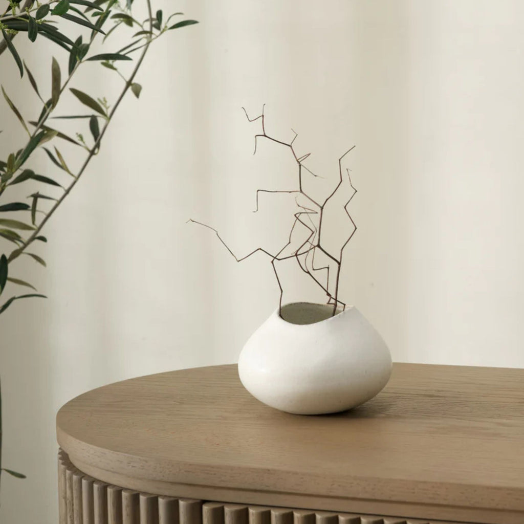 White vase with branches on a wooden table against a beige wall