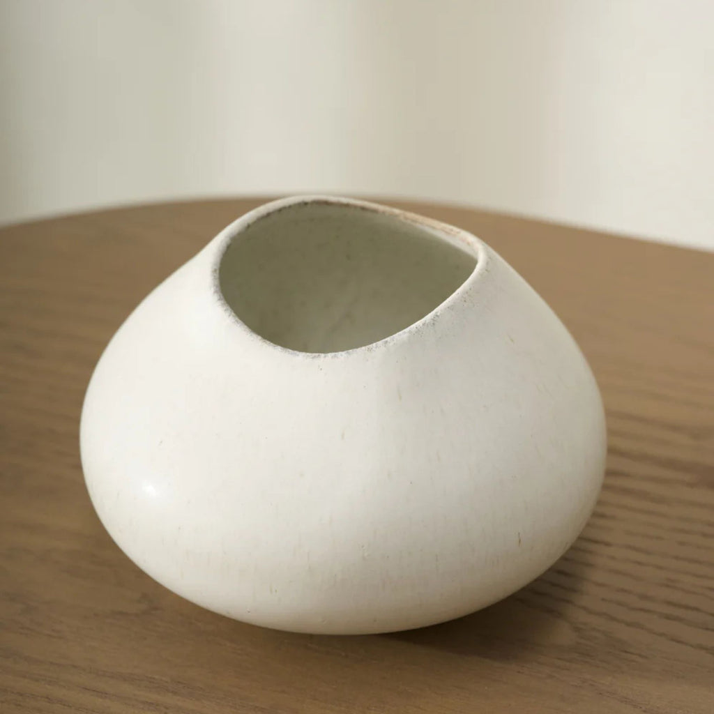 White ceramic vase on a wooden surface with a plain background