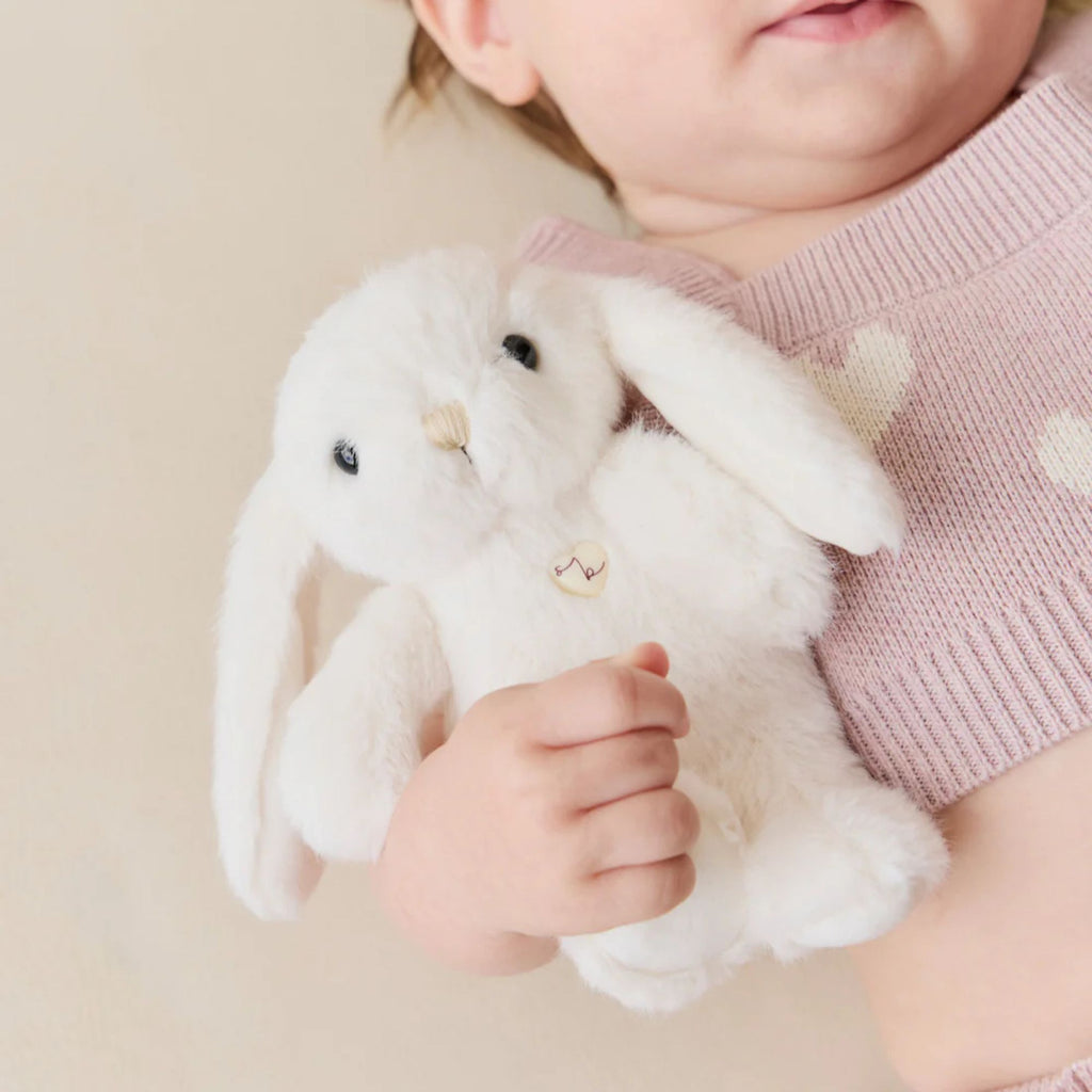Child holding a fluffy white toy rabbit against a neutral background