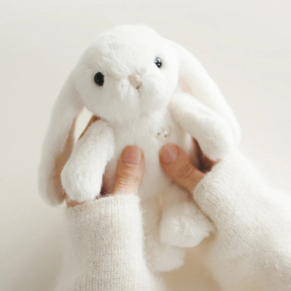 White plush bunny held by a person against a light background
