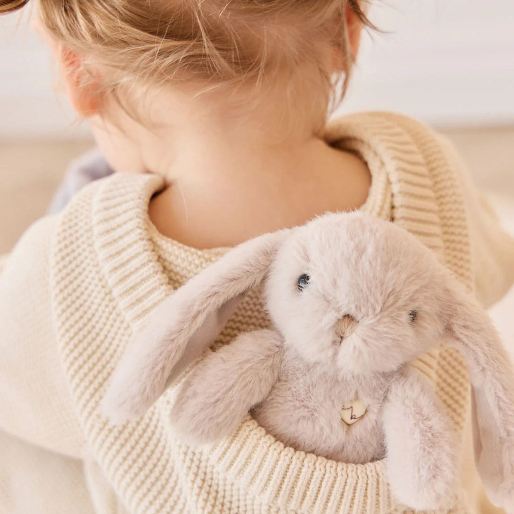 Child holding a plush bunny toy wrapped in a beige sweater