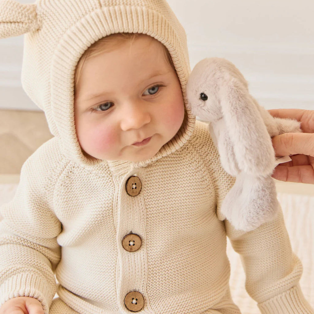 Baby in a beige knitted bunny outfit holding a plush toy