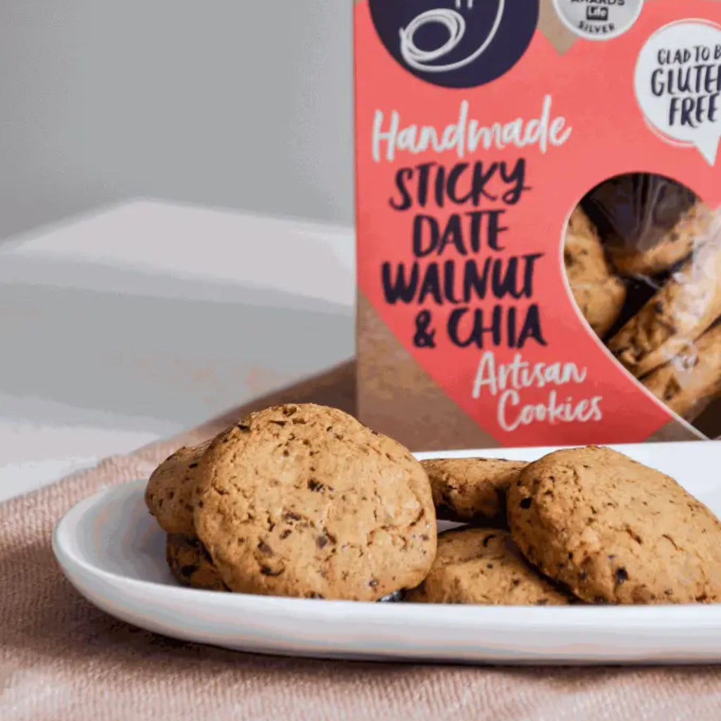 Box of handmade sticky date walnut & chia cookies with cookies on a plate in front