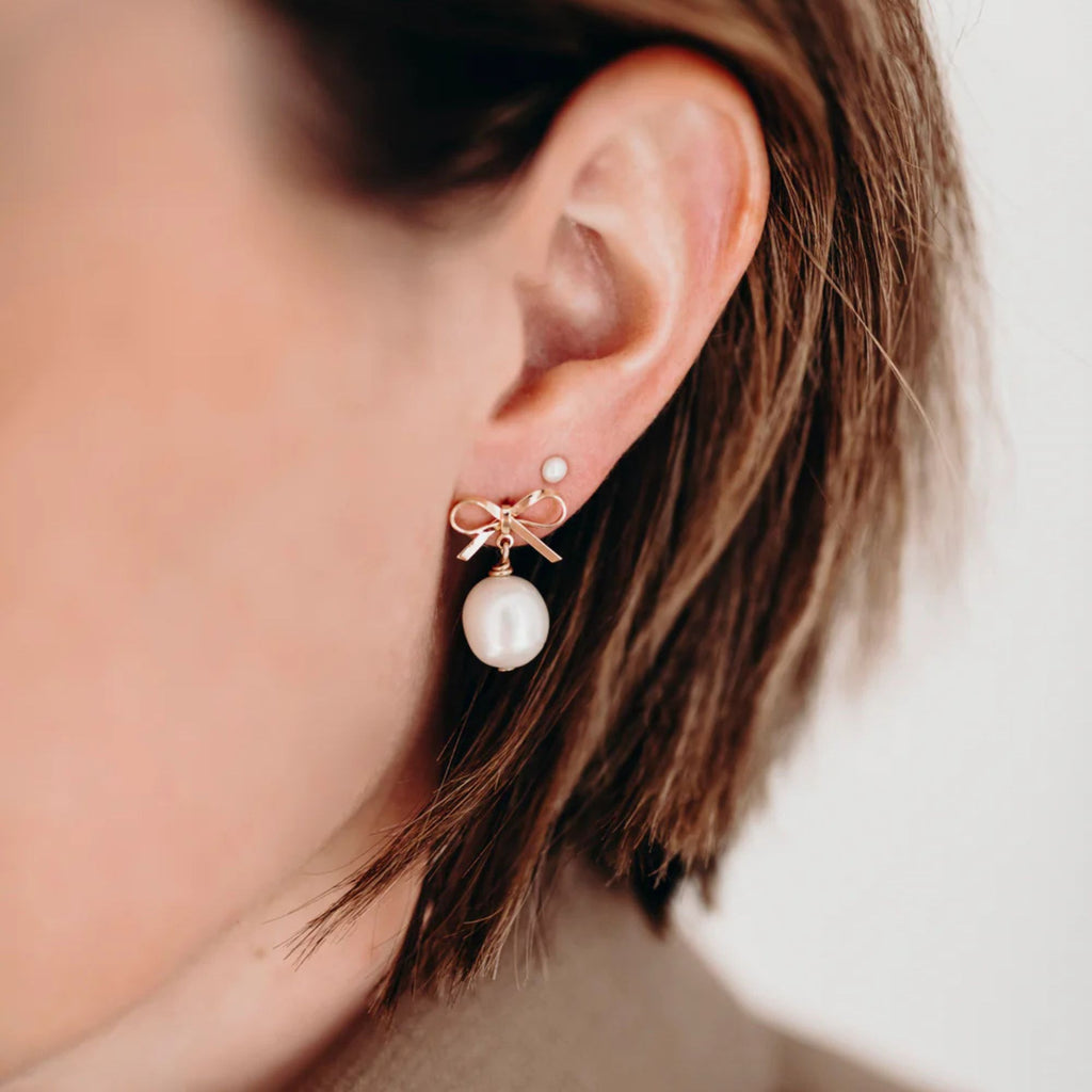 Close-up of an ear wearing a gold earring with a pearl drop against a neutral background