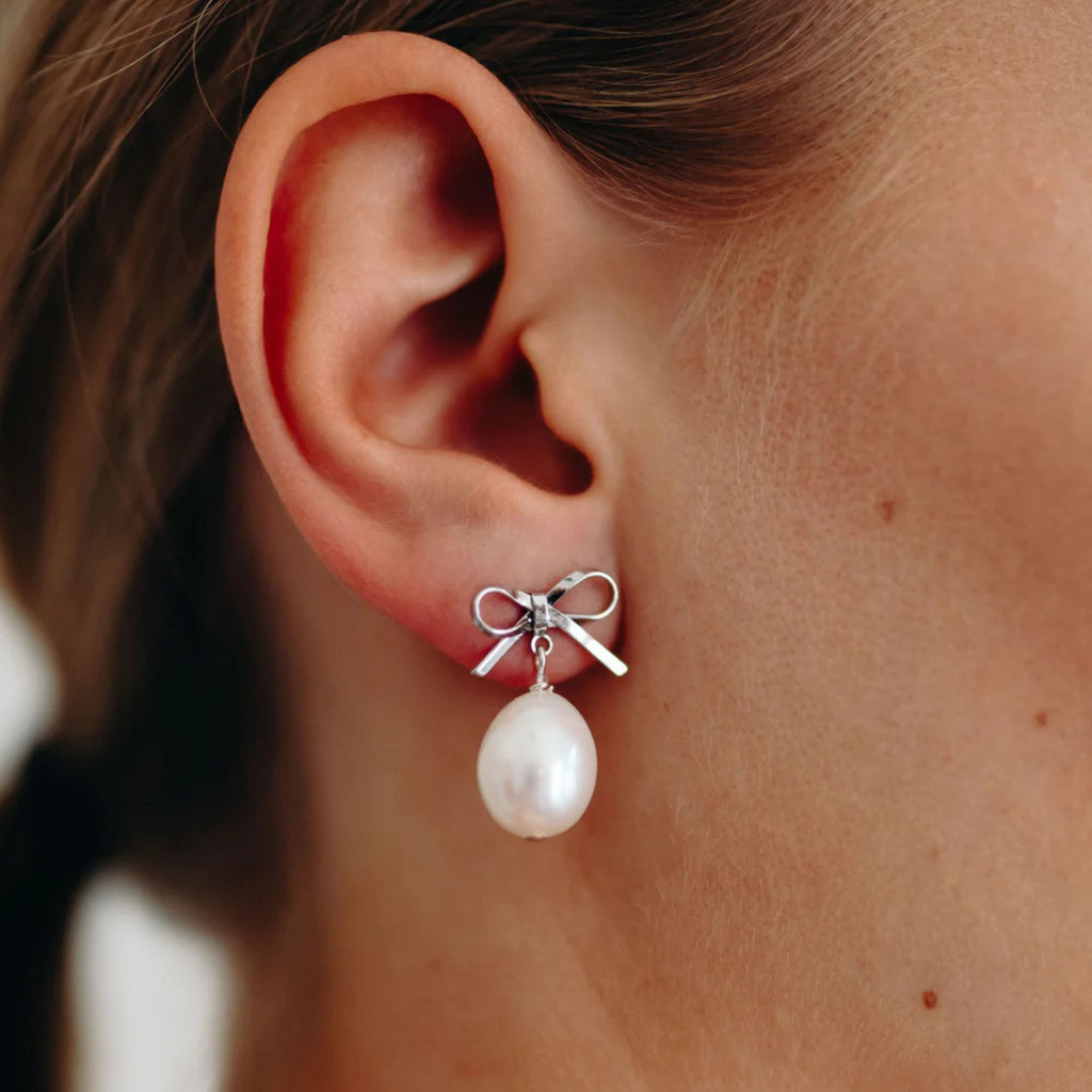 Pearl earring with bow detail on an ear against a blurred background