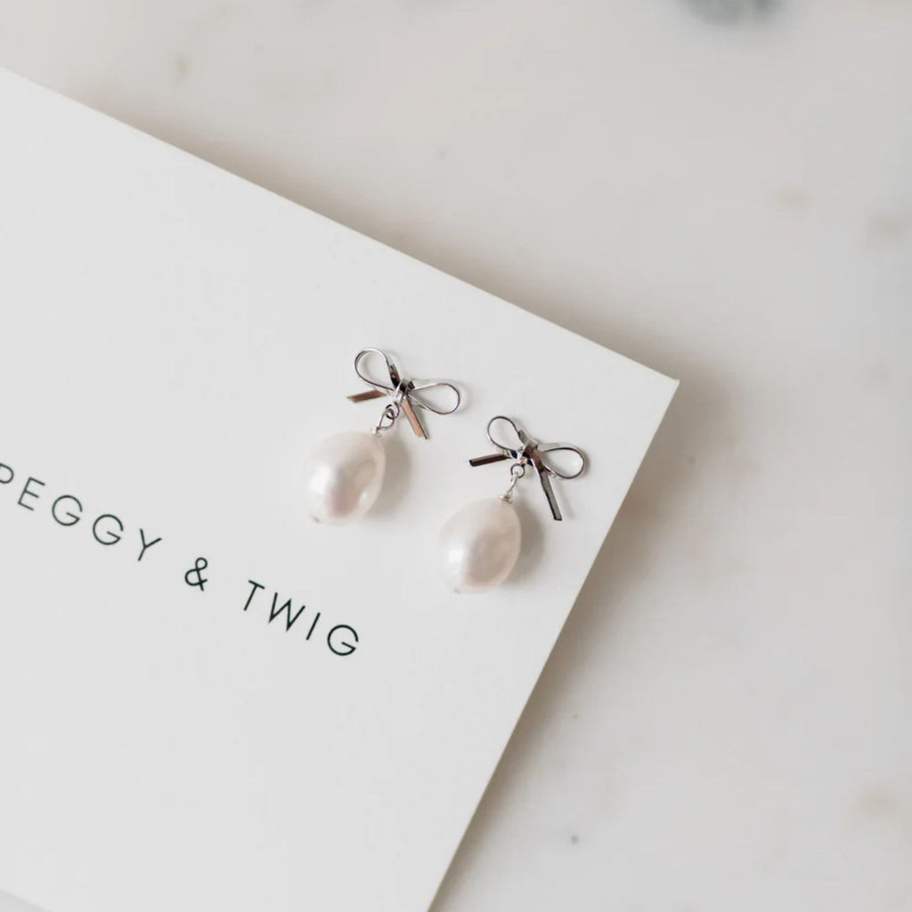 Pearl earrings with silver bows on a white card with 'Peggy & Twig' branding.
