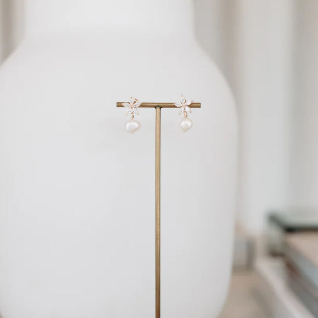Pearl earrings on a gold stand against a white background