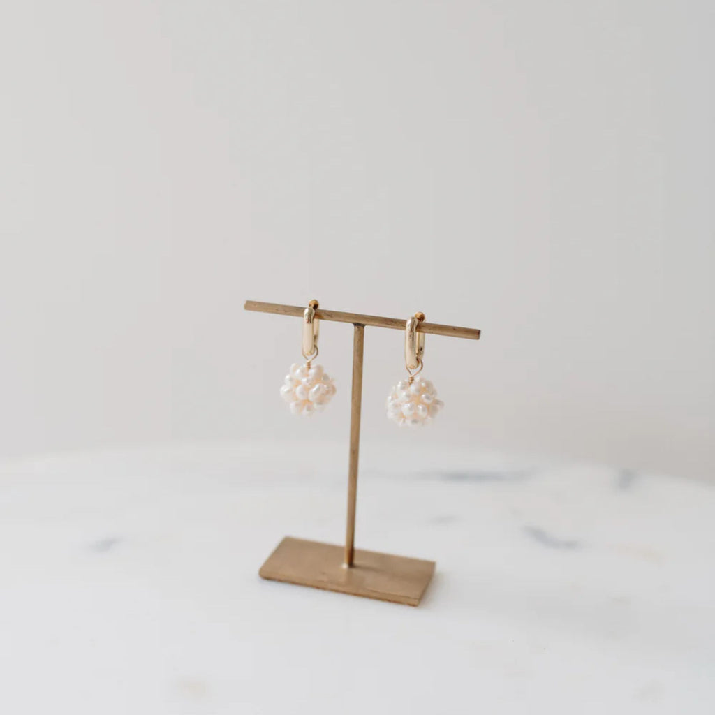 Gold earring stand with two pearl earrings on a light gray background
