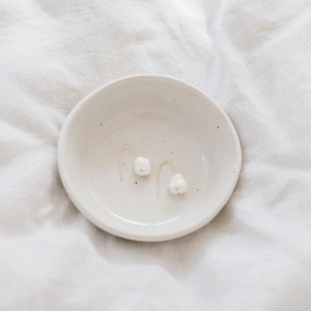 White ceramic dish with two pearls on a white fabric background